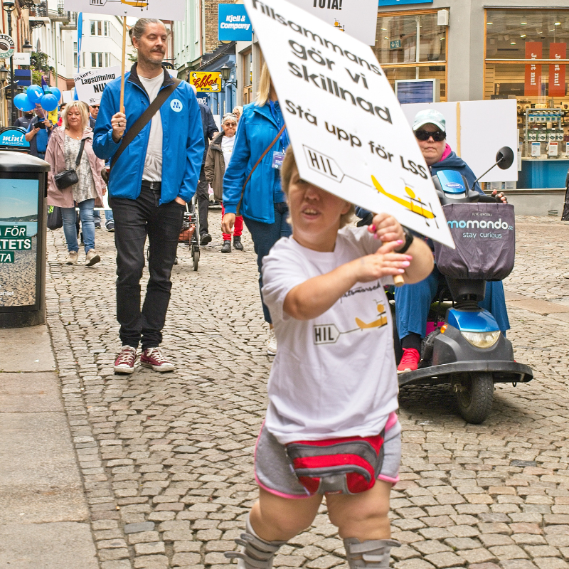 Bilden visar en kvinna som marscherar och bär plakatet med texten, Tillsammans gör vi skillnad. Stå upp för LSS