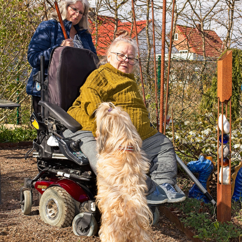 Bilden visar Anki i sin trädgård med hunden och sin personliga assistent. Som assistent är att finnas till hands utan att ta plats