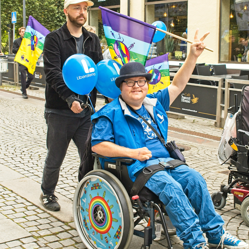 William marscherar sittande i sin rullstol som hans personliga assistent kör